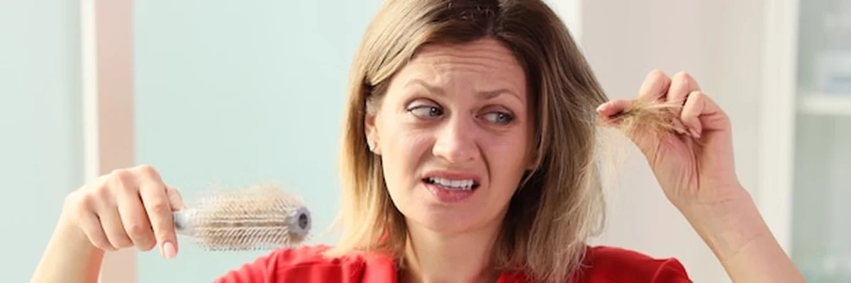 Kobieta z szczotką do włosów patrząca na osłabione i wypadające włosy