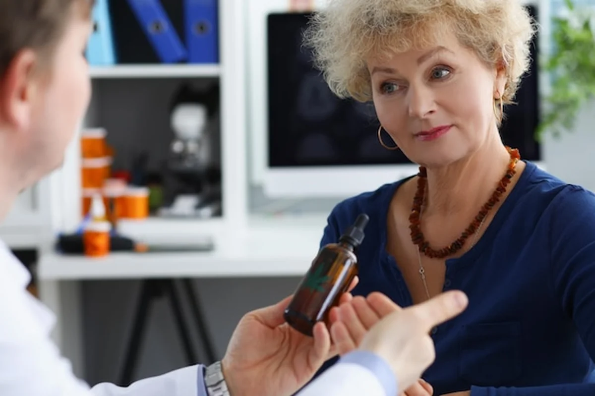 Lekarz podaje starszej kobiecie butelkę z olejem z konopi indyjskich