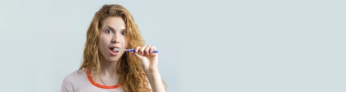 Uśmiechnięta kobieta z czerwonymi włosami trzymająca szczoteczkę do zębów na białym tle