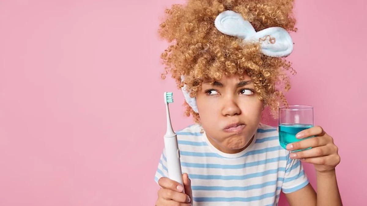 Młoda kobieta myjąca zęby elektryczną szczoteczką i płynem do płukania ust