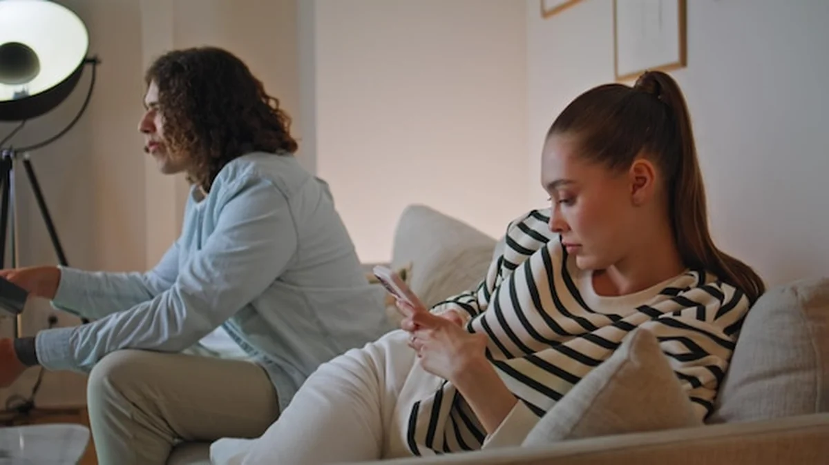 Frustrowana para na kanapie wieczorem; oddzielona kobieta pisząca SMS-y