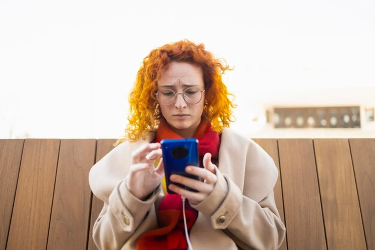 Młoda kobieta zmartwiona czyta wiadomości na smartfonie