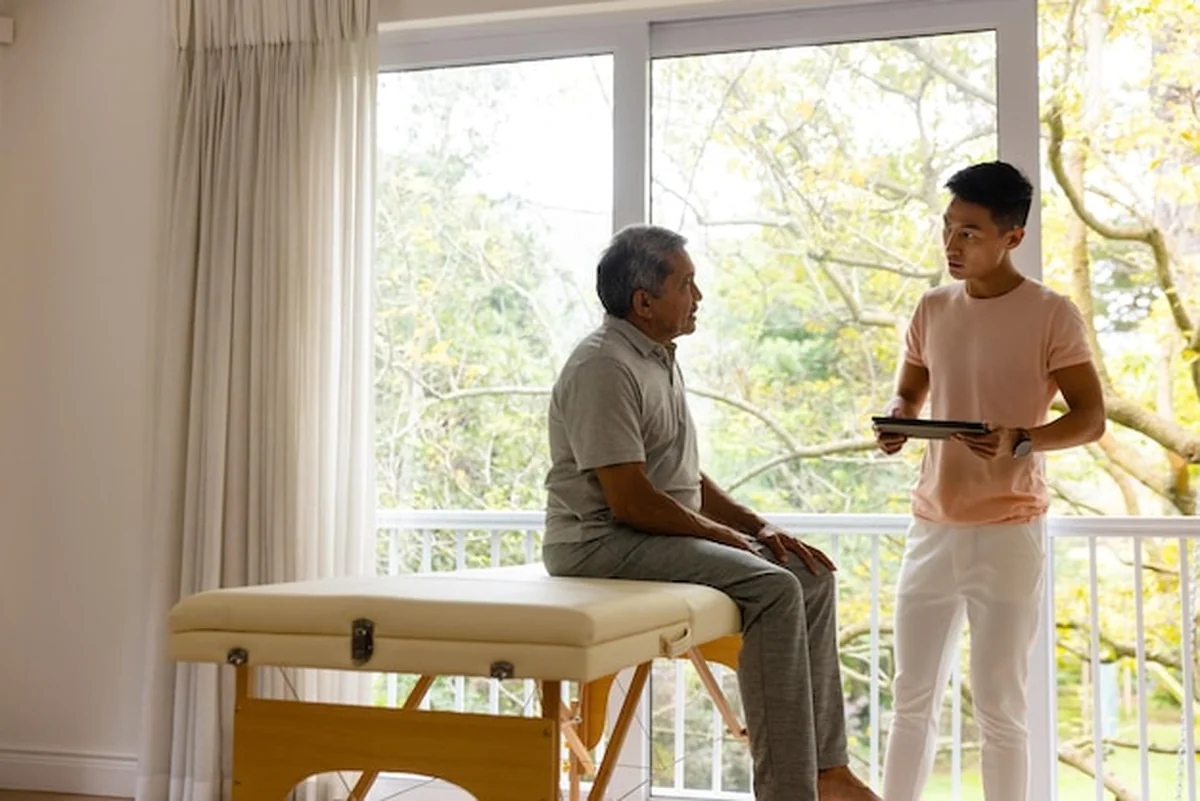 Fizjoterapeuta bada starszego pacjenta z tabletem