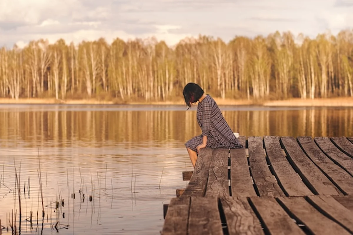 Młoda dziewczyna siedzi na molo w letniej sukience