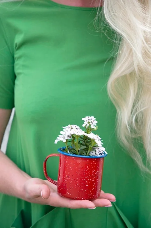 Blondynka z długimi włosami w jasnozielonej sukience trzymająca czerwony kubek