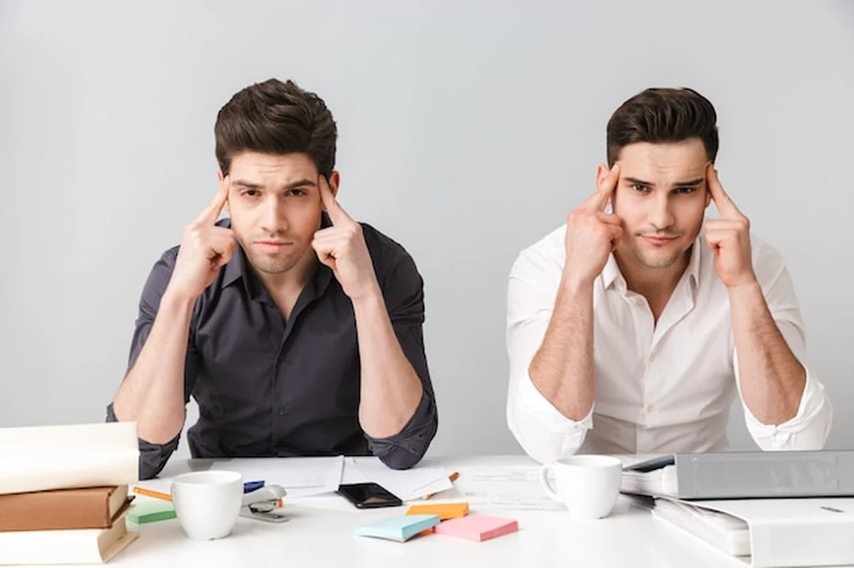 Dwóch młodych biznesmenów w coworkingu, jeden zmęczony, drugi szuka aparatu