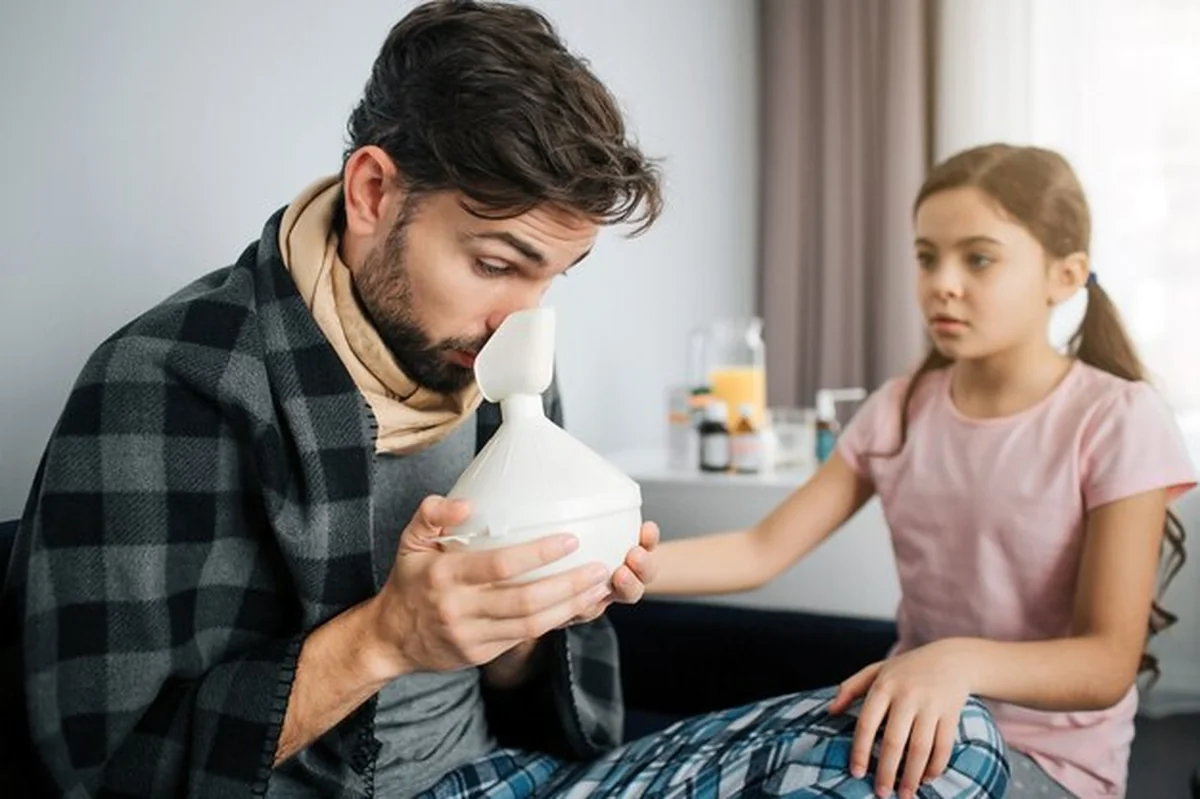 Chory młody człowiek robi inhalacje, zmartwiona dziewczynka obok
