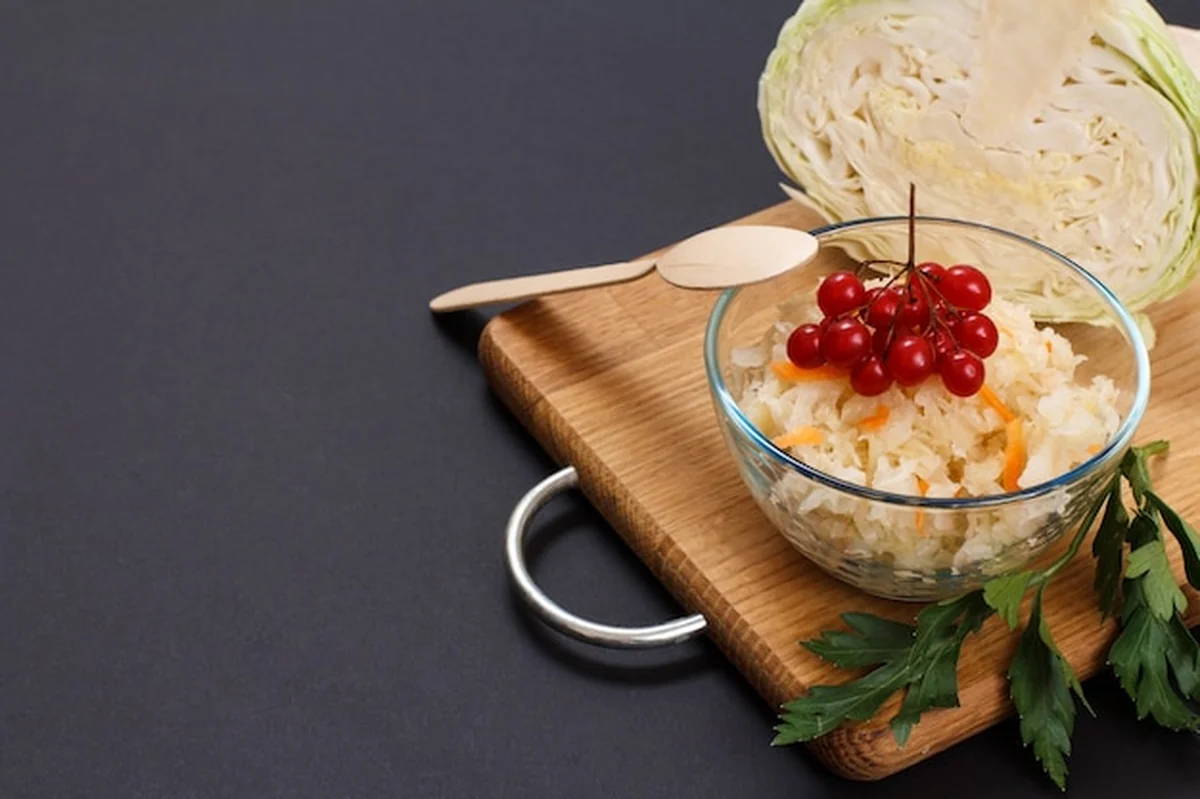 Kiszona kapusta z warzywami w misce, drewniana łyżka, świeża kapusta na tle. Sałatka wegańska bogata w witaminę U