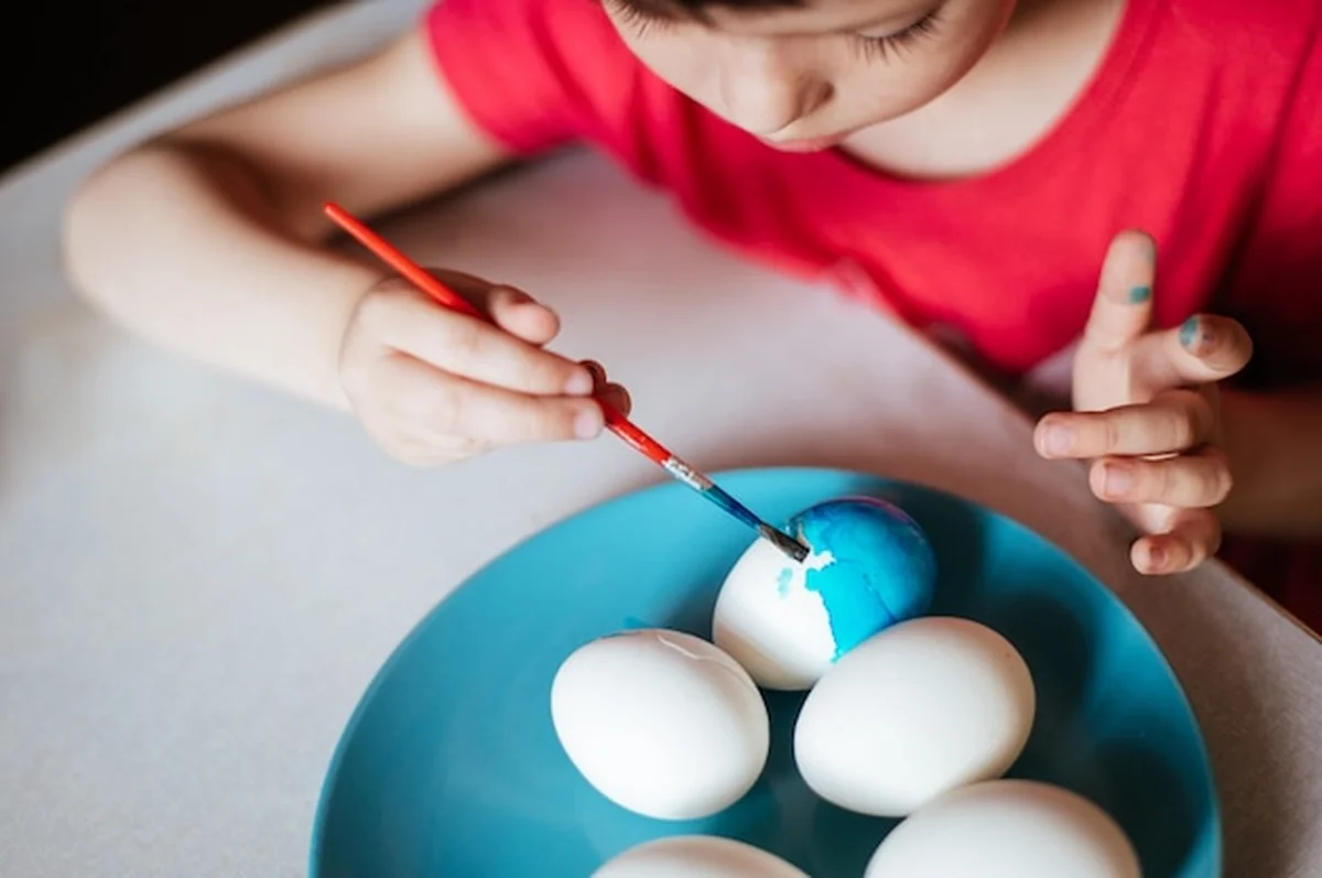 Dziewczynka maluje jajka przy stołu na błękitnym naczyniu